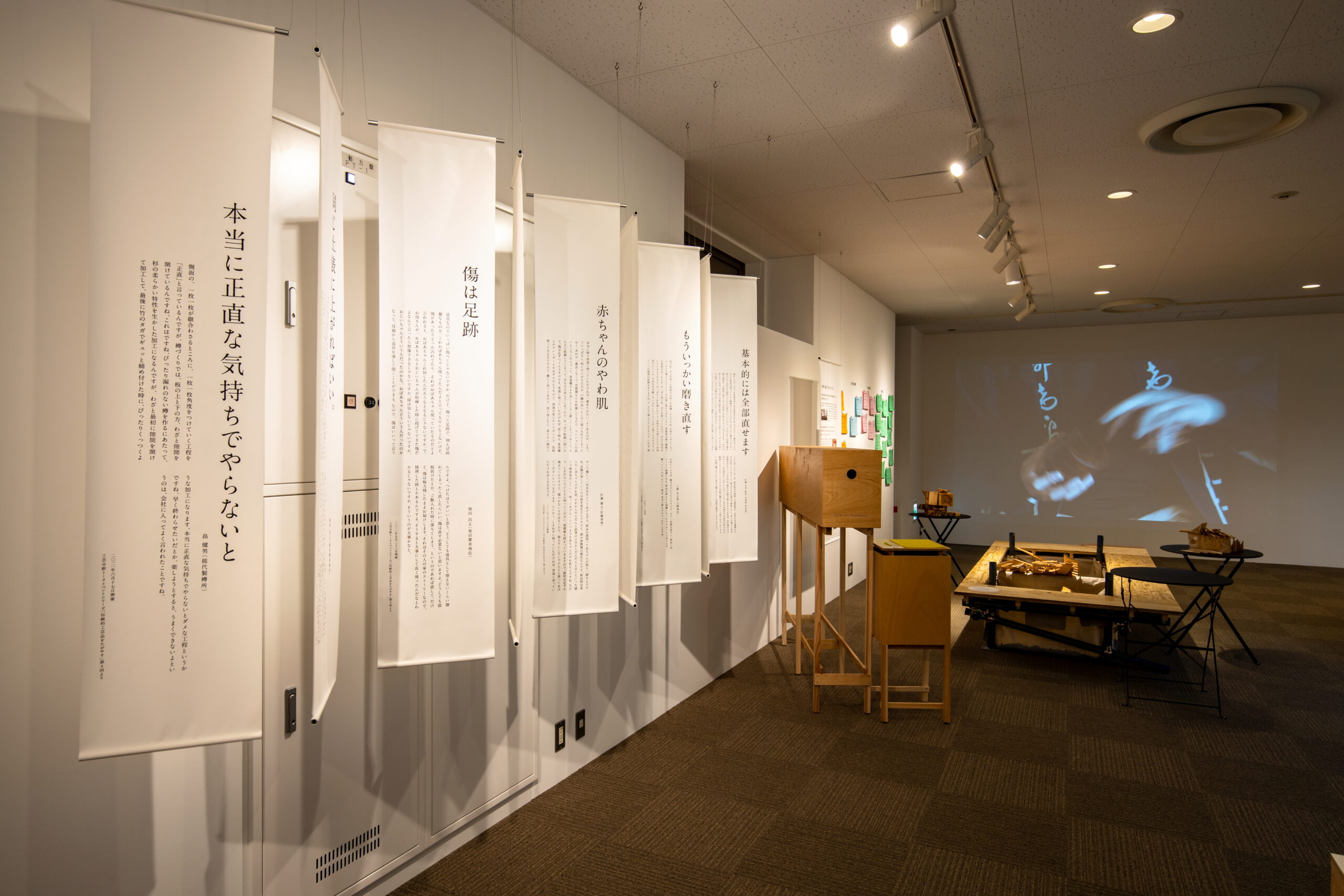 修繕をめぐる言葉を綴った布バナーが吊るされた展示空間と、職人の手元を映す映像インスタレーション