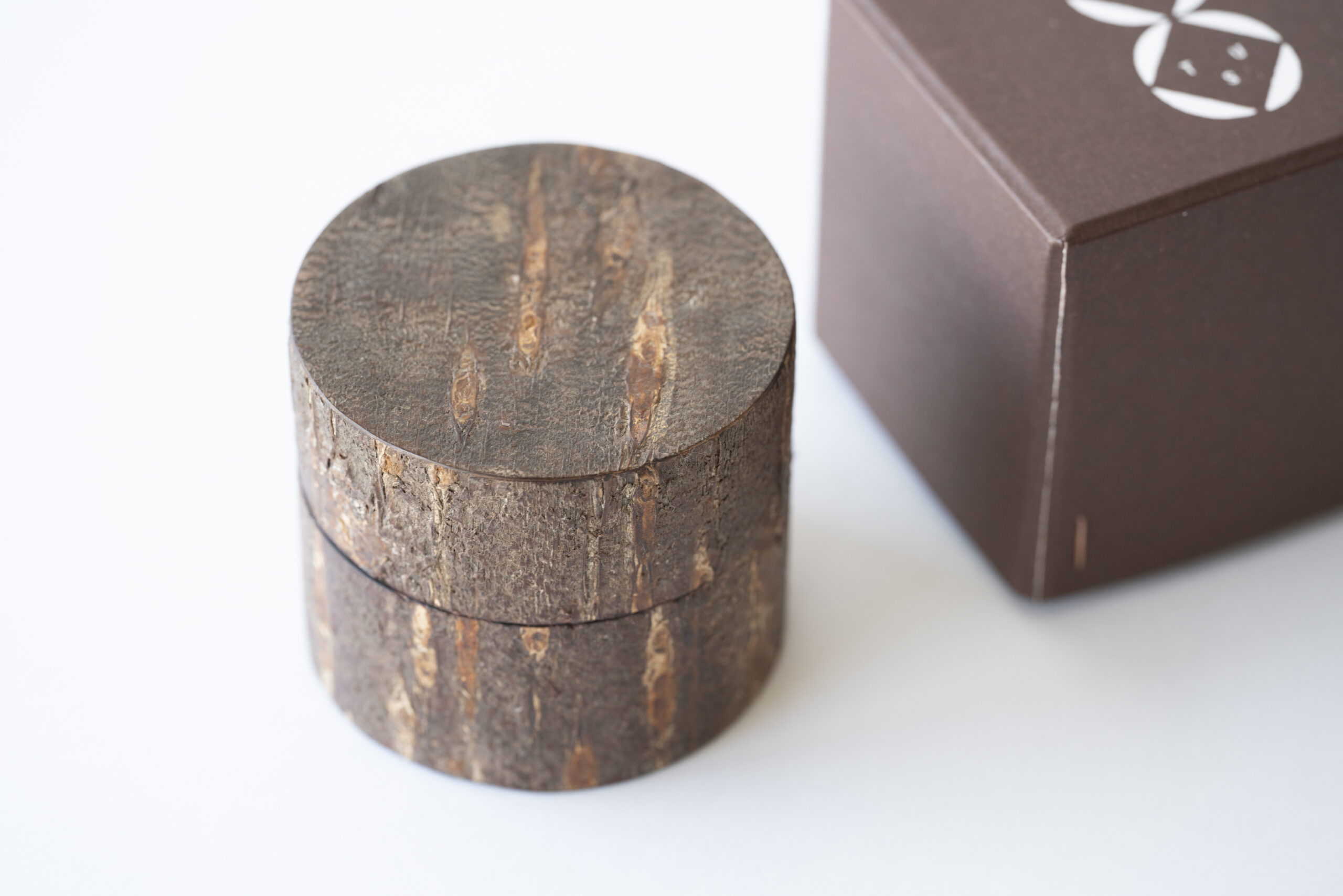 樹皮そのものの表情を活かした丸い茶筒と、ブランドのパッケージ箱