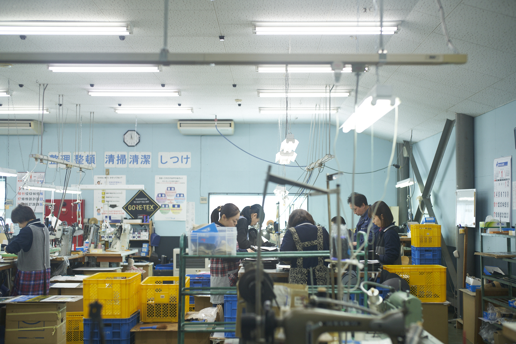 靴工場の作業風景(スタッフが並んで作業する明るい工場内)