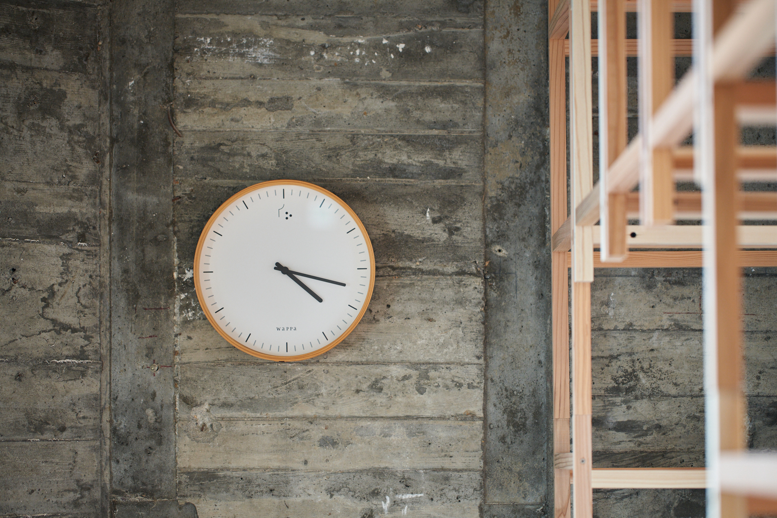 コンクリートの壁に掛けられたWa CLOCKと、木材の建材が並ぶ空間