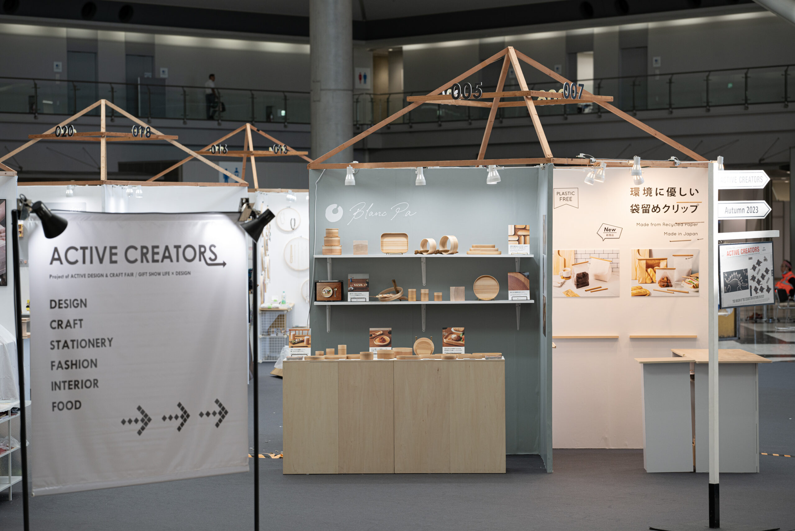 秋田杉の端材を組んだ屋根型の什器と、商品を並べた棚を見せるブース全景