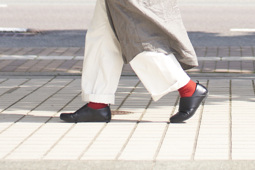 赤い靴下がのぞく着こなしで靴を履いて歩く様子